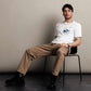 Man sitting on a chair wearing a white Christian t-shirt and beige pants against a plain background