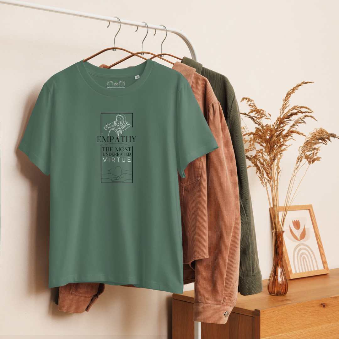 Green t-shirt with text on a hanger against a neutral wall with a wooden dresser and decorative items.