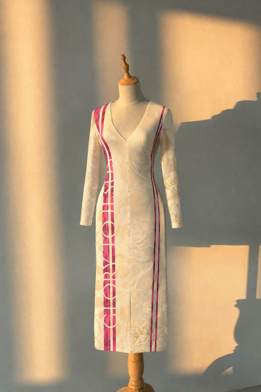 A long-sleeve V-neck midi dress displayed on a wooden dress form. The dress is off-white with a subtle jacquard pattern, featuring bright pink vertical side panels and piping details.