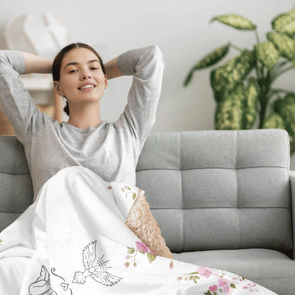 A person relaxing on a couch, covered with a sherpa blanket featuring a floral design with ornaments in the center.