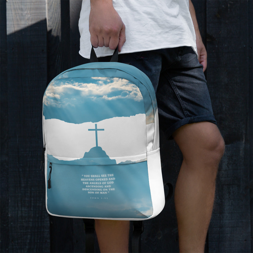 Person holding backpack featuring a blue sky with a cross and clouds design, and a quote from the Bible.
