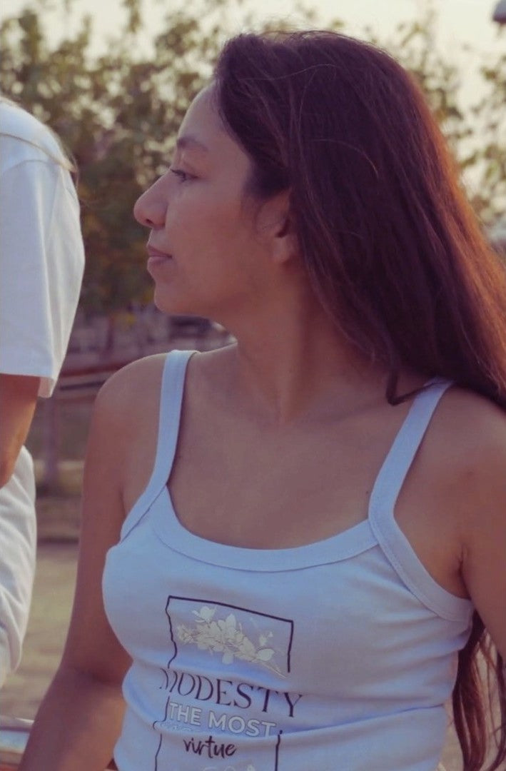 Woman wearing a white tank top with text outdoors