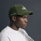 Person wearing a green cap with a logo on a dark background