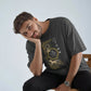 Man wearing a dark t-shirt with a graphic design, sitting on a wooden stool against a light background