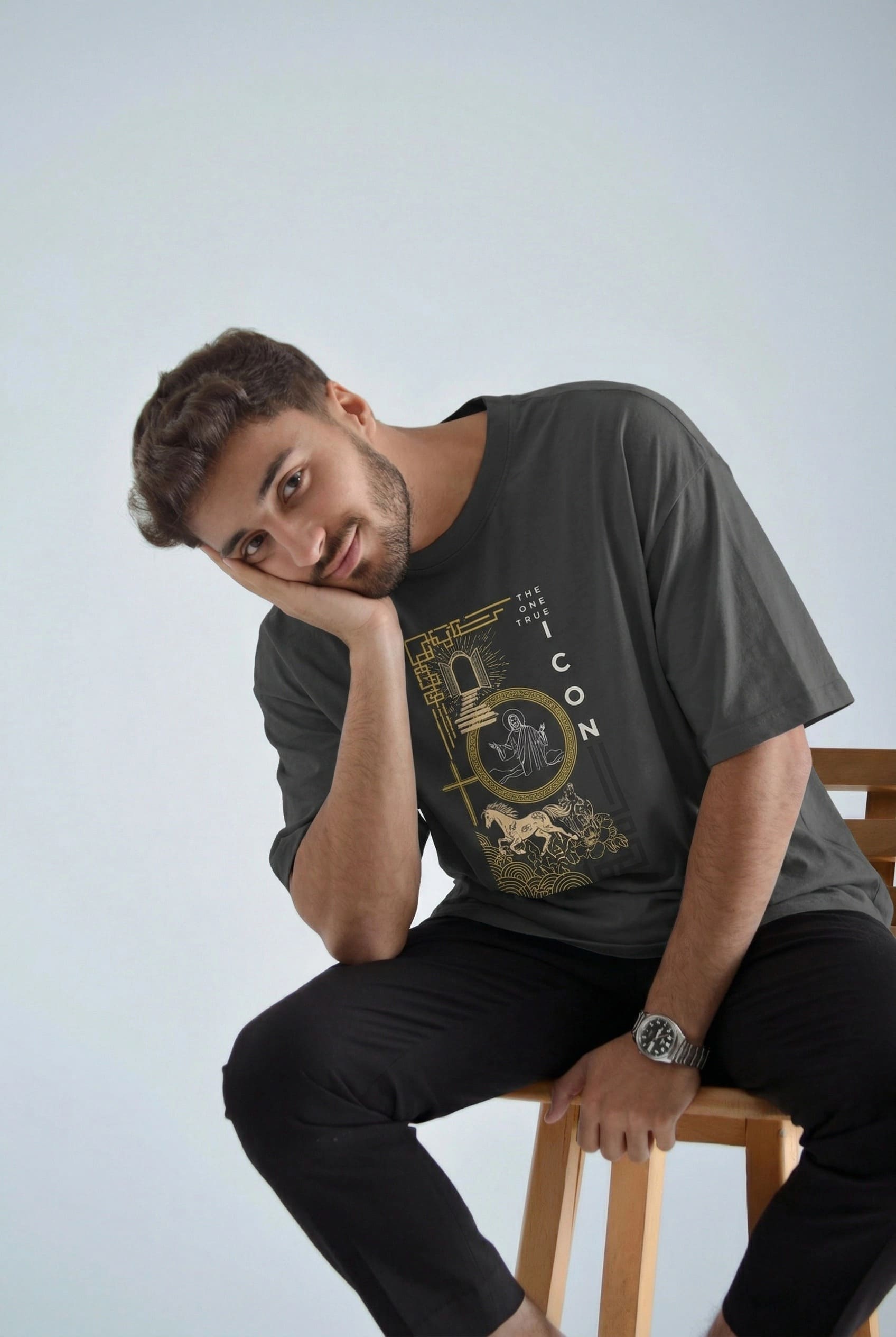 Man wearing a dark t-shirt with a graphic design, sitting on a wooden stool against a light background