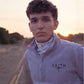 Person wearing a gray sweater with 'FAITH' printed on it, standing in a nature landscape at sunset.