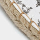 Close-up of a woven textile product showing a white fabric base with a black floral toile pattern and a thick braided natural jute rope trim bound by tan thread.