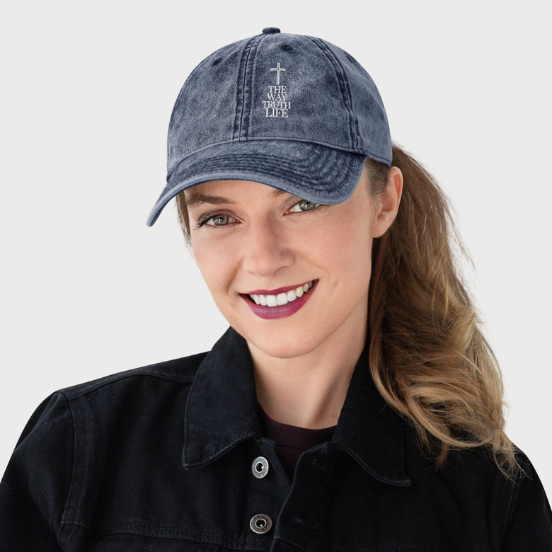 Woman wearing a blue denim cap with a cross and text on a plain background