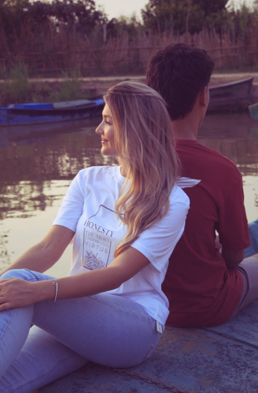 Two people sitting by a body of water with boats in the background.